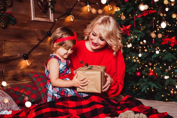 God Jul och Gott Nytt År! Mor ger presentask till ett barn i vardagsrummet dekorerat med julgran och julklappslådor. Porträtt kärleksfull familj på nära håll, semester — Stockfoto