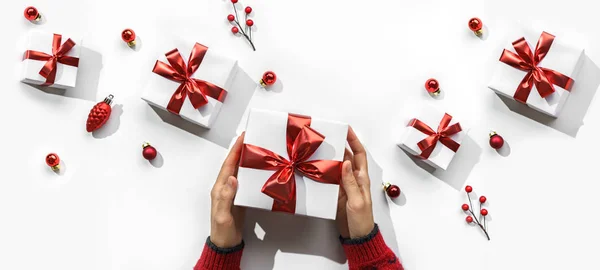 女性的手拿着白色背景的圣诞礼品盒，有冷杉枝条，红色装饰，闪烁着火花和彩霞。圣诞和新年贺卡,寒假.平躺在地上，俯瞰四周 — 图库照片
