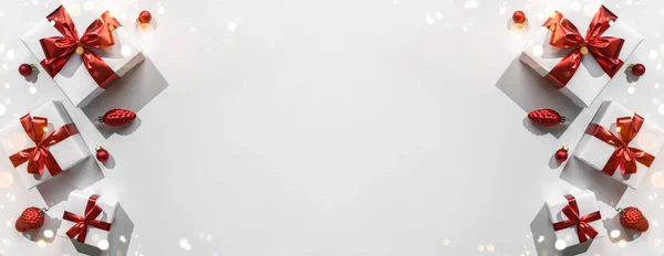 Χριστουγεννιάτικα κουτιά δώρου με κόκκινη κορδέλα και διακόσμηση σε λευκό φόντο με bokeh, φως. Χριστούγεννα και καλές πρωτοχρονιάτικες διακοπές. Επίπεδο lay, κορυφαία άποψη, σκληρή σκιά — Φωτογραφία Αρχείου