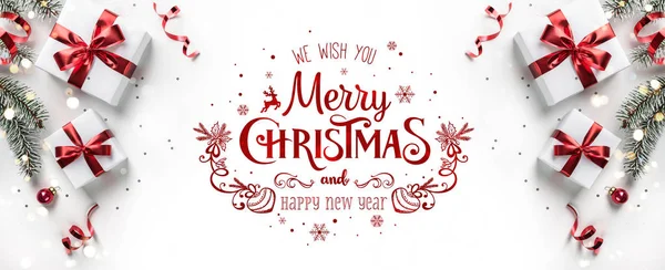 ギフトボックス、リボン、赤い装飾、モミの枝、ボケ、輝きとコンフェッティと白い背景にメリークリスマステキスト。クリスマスと新年の挨拶カード、ボケ、光。フラットレイアウト、トップビュー — ストック写真