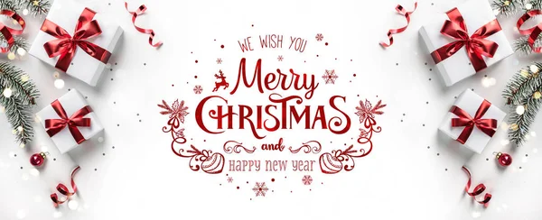 Hediye kutuları, kurdeleler, kırmızı süslemeler, köknar dalları, bokeh, pırıltı ve konfeti içeren beyaz arkaplan üzerine Mutlu Noeller metni. Xmas ve yeni yıl tebrik kartı, bokeh, ışık. Düz yatış, üst görünüm