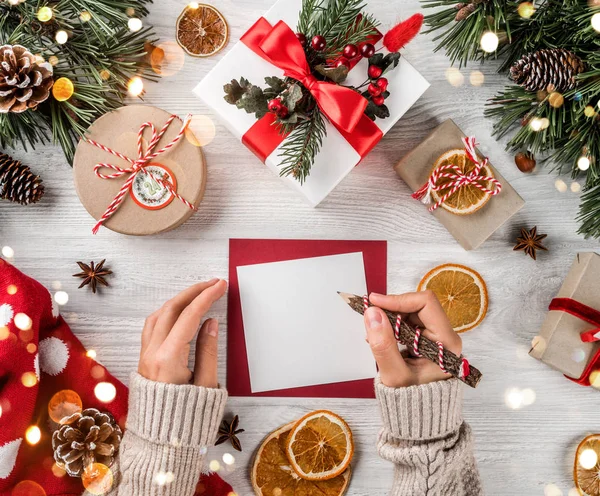 白地クリスマス プレゼント、モミの枝、セーター、マツ円錐形で木製のサンタさんへ手紙を持つ女性の手。テーマはクリスマスと新年あけましておめでとうございます。フラット横たわっていた、トップ ビュー — ストック写真