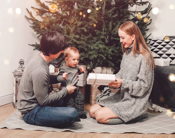 Glad familj par ger gåvor i vardagsrummet, bakom den dekorerade xmas trädet, ljuset ger en mysig atmosfär. Nytt år och god jul — Stockfoto