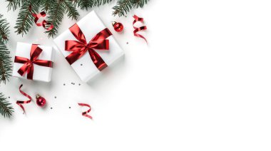 Noel ağacı dalları, kırmızı kurdeleli hediye kutuları, kırmızı süslemeler, parıltılar ve beyaz arka planda konfeti. Noel ve yeni yıl tebrik kartı, kış tatili. Düz yatış, üst görünüm