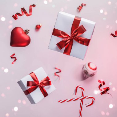 Uçan süslemeler, hediye kutuları, kırmızı süslemeler, toplar, pırıltılar ve açık pembe arka planda konfetilerden oluşan mutlu noel kartları. Noel ve Yeni Yıl tatili, Bokeh, ışık. Seçici odak