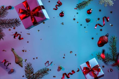 Uçan süslemeler, hediye kutuları, köknar dalları, toplar, ışıltılar ve renkli neon ve mor arka planda konfetilerden oluşan Noel kartı. Xmas ve yeni yıl tatili, bokeh, ışıklar. Seçici odak
