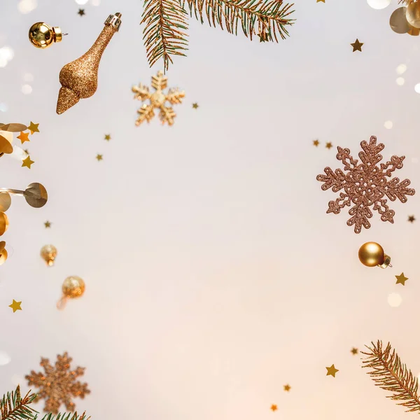 Creative frame made of flying Christmas decorations, gold fir branches, balls, snowflakes, sparkles and confetti on light gold background. Xmas and New Year holiday, bokeh, light. Selective focus — Stock Photo, Image