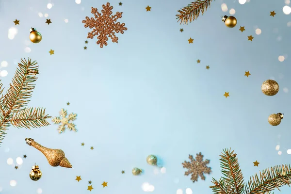 Moldura criativa feita de decorações de Natal voadoras, ramos de abeto de ouro, bolas, flocos de neve, brilhos e confetes no fundo azul claro. Natal e feriado de Ano Novo, bokeh, luz. Foco seletivo — Fotografia de Stock