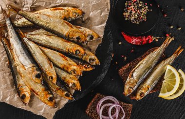 Smoked fishes sprat marinated with spices, salt, greens and slice of bread on plate over dark stone background. Mediterranean food, appetizer, seafood, top view clipart