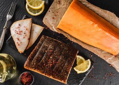 Baharatlı ve yağlı füme beyaz fileto balığı. Esmer taş arka planda el işi kağıt üzerinde. Deniz ürünleri, üst manzara.