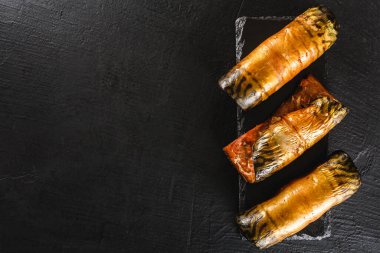 İştah açıcı füme uskumru balıklı börekler, baharatlar, biber ve ekmek, arka planda koyu bir sayfa. Akdeniz yemeği, ringa balığı, deniz ürünleri, üst manzara.