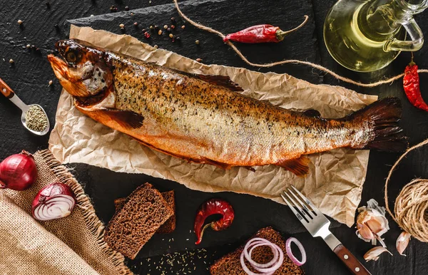Smoked trout fish, red whole fish with spices and onion on craft paper over dark stone background. Seafood, top view — Stock Image Smoked Trout Fish Red Whole Fish Spices Onion Craft Paper Stock Picture