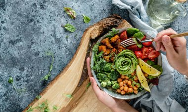 Ellerinde sağlıklı bir süper kase salata, fırında tatlı patates, nohut, brokoli, humus, avokado, ahşap tahtada filizlenen Buda kasesi. Sağlıklı vejetaryen yemekleri, temiz yemek, perhiz, üst manzara.