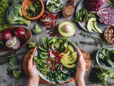 Kadın avokado, yeşillik, roka ve gri arka planda ıspanak ile sağlıklı taze salata pişiriyor. Sağlıklı vejetaryen yemekleri, temiz yemek, diyet, üst görünüm, ton.