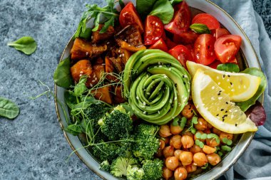 Fırında patates, nohut, brokoli, domates, yeşillik, avokado, açık mavi arka planda bezelye filizi ve peçete. Sağlıklı vejetaryen yemekleri, temiz yemek, perhiz, üst manzara.