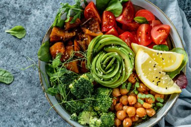 Buddha bowl salad with baked sweet potatoes, chickpeas, broccoli, tomatoes, greens, avocado, pea sprouts on light blue background with napkin. Healthy vegan food, clean eating, dieting, top view clipart