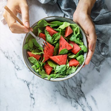 Elleri sağlıklı taze karpuz salatası, roka, ıspanak ve açık mermer arka planda yeşillikler tutuyor. Sağlıklı yemek, temiz yemek, Buda kasesi salatası, üst manzara.