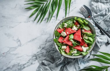 Feta peynirli taze karpuz salatası, roka, ıspanak ve açık mermer arka planda tropikal yapraklı yeşiller. Sağlıklı yemek, temiz yemek, Buda kasesi salatası, üst manzara.