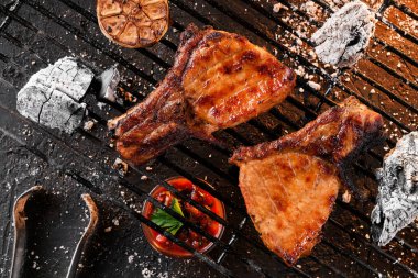 Kömürün üstünde sarımsaklı ızgara T-Bone bifteği, ateş ışığında koyu bir arka plan. Üst görünüm