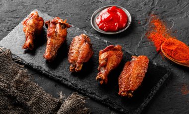 Izgara tavuk kanadı ve bacaklar et ve domates sosu koyu arkaplanda tahtada. Üst görünüm