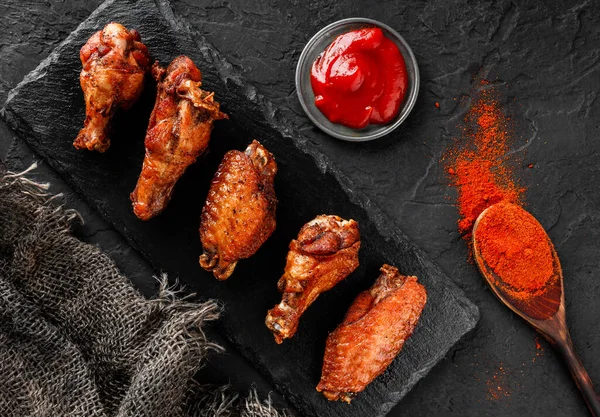 烤鸡翅和腿肉与番茄酱在板板上的深色背景 顶部视图 — 图库照片