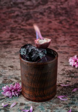 Votka, buz ve ahşap bardaktaki tutkulu meyveli taze tropik alkollü kokteyl ve dokulu arka planda alev. Soğuk yaz içeceği ve kokteyl