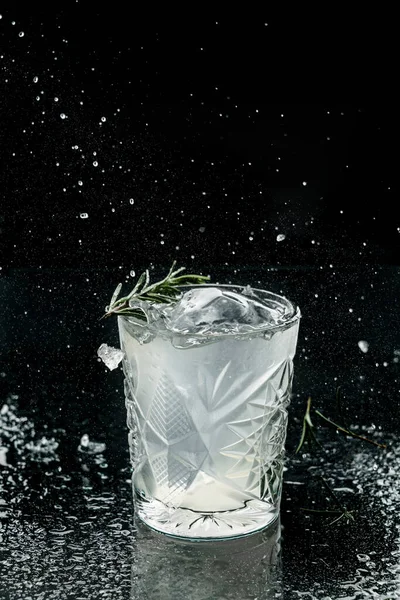 ウォッカ アイス ローズマリーをガラスに黒を基調にしたフレッシュアルコールカクテル 凍結運動中の飲み物のスタジオショット 氷と滴を飛んで 夏の冷たい飲み物とカクテル — ストック写真