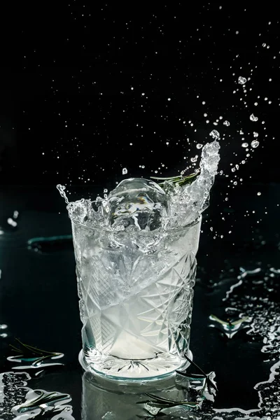 ウォッカ アイス ローズマリーをガラスに黒を基調にしたフレッシュアルコールカクテル 凍結運動中の飲み物のスタジオショット 氷と滴を飛んで 液体スプラッシュ 夏の冷たい飲み物とカクテル — ストック写真