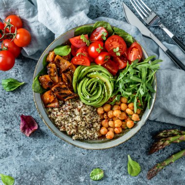 Fırında patates, nohut, kinoa, domates, roka, avokado, açık mavi arka planda peçeteli lahanalı Buda kasesi salatası. Sağlıklı vejetaryen yemekleri, temiz yemek, perhiz, üst manzara.