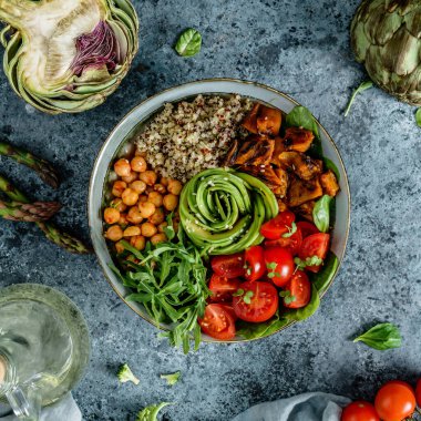 Fırında patates, nohut, kinoa, domates, roka, avokado, açık mavi arka planda peçeteli lahanalı Buda kasesi salatası. Sağlıklı vejetaryen yemekleri, temiz yemek, perhiz, üst manzara.