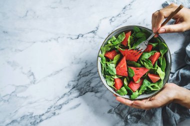 Elleri sağlıklı taze karpuz salatası, roka, ıspanak ve açık mermer arka planda yeşillikler tutuyor. Sağlıklı yemek, temiz yemek, Buda kasesi salatası, üst manzara.