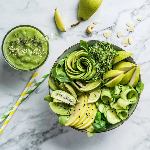 Fresh summer salad with avocado, kiwi, apple, cucumber, pear, micro greens, lime and sesame with smoothie on light marble background. Healthy food, clean eating, Buddha bowl salad, top view