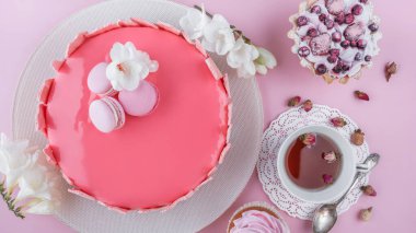 Makaronlarla süslenmiş ayna jöleli pembe kremalı pasta, pembe tatil arka planında Mutlu Yıllar için çiçekler. Tatil pastası kutlaması. Üst manzara, düz uzanma