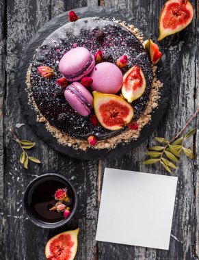 Aynalı kremalı çikolatalı pasta. Makaronlarla, incirlerle, koyu kırsal arka planda çiçeklerle süslenmiş. Kağıt kartla tatil pastası kutlaması. Üst manzara, düz uzanma