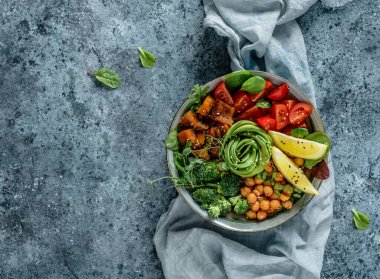 Fırında patates, nohut, brokoli, domates, yeşillik, avokado, açık mavi arka planda bezelye filizi ve peçete. Sağlıklı vejetaryen yemekleri, temiz yemek, perhiz, üst manzara.