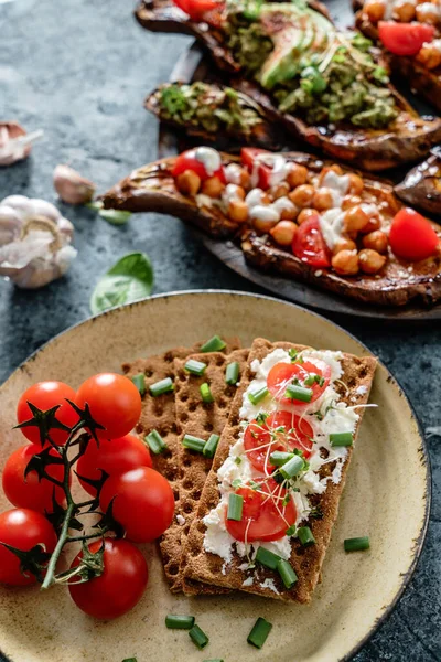 Rye bread toasts with goat cheese, tomatoes, seedlings on plate on blue background with baked sweet potato toast with roasted chickpeas, avocado. Healthy vegan food, clean eating, dieting, closeup