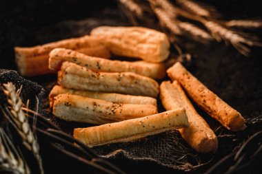 Kırsal arka planda susamlı puf ekmeği çubukları ve buğday dikenli kumaş. Pastalar ve pastane, kapatın.