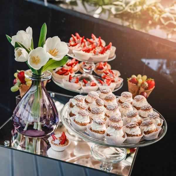 Wedding dessert, macaroons, meringues, cupcakes, muffins, cakes and sweetness on holiday background with flowers. Candy bar