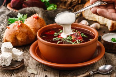 Ukrayna ve Rusya 'nın geleneksel pancar çorbası ya da pirzola eti, çörek ve ahşap arka planda maydanozlu borş çorbası. Elleri pancar çorbasında kaşıktan ekşi krema döküyor. Sağlıklı yiyecekler, kapatın.