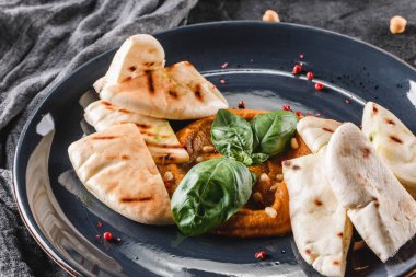 Gri arka planda seramik tabakta zeytinyağı, paprika, çam fıstığı ve pita ekmeği ile nohut. Sağlıklı vejetaryen yemekleri, temiz yemek, perhiz, üst manzara.