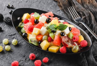 Koyu arkaplanda tekstil ve böğürtlenli taze meyve salatası manzarası, yakın çekim. Sağlıklı kahvaltı, kilo verme konsepti