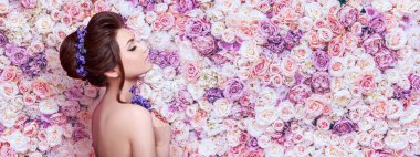 Beauty young woman with flowers in hair on background wall of flowers. Perfect face skin and Fashion makeup. Beautiful Woman Portrait. Hair care concept clipart