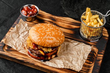 Lezzetli burger, ananas dilimleri, et pirzolası, tahta tahtada bir dilim peynir ve sos ve siyah arka planda patates kızartması. Fast food öğle yemeği, üst manzara.