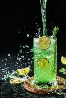 Limonlu, biberiyeli, naneli ve buzlu mojito kokteyli koyu arkaplanda. Stüdyo çekiminde, dondurucu hareketle içki, sıvı sıçraması. Soğuk yaz içeceği ve kokteyl