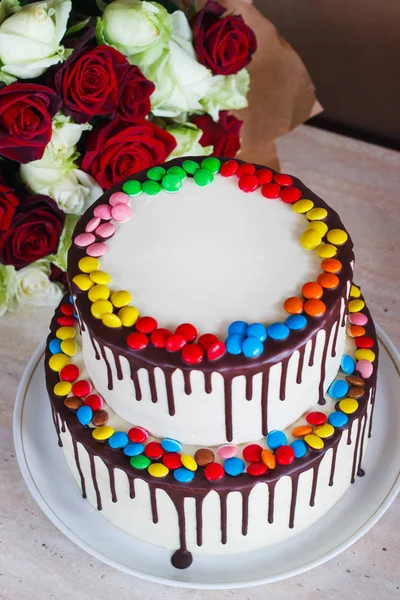 White Birthday cake with colorful Sprinkles over a light background with a bouquet of roses — Stock Photo, Image