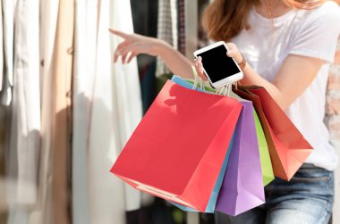 Alışveriş kız elinde alışveriş çanta ile smartphone ve diğer el kıyafet seçimi.