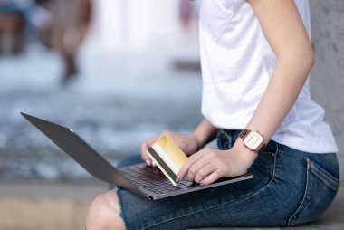 Kredi kartı tutan alışveriş kızlar dizüstü bilgisayar kullanıyorsanız. O oturdu ve bacak üzerinde koymak laptop.