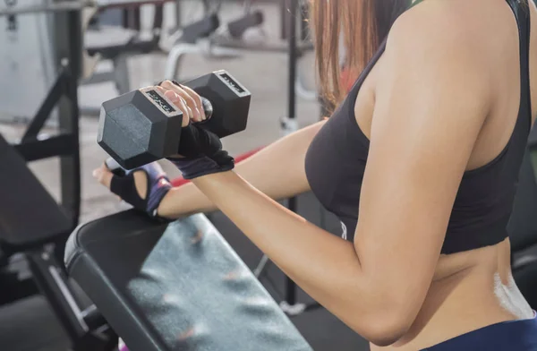 Fitness woman lifting dumbbell in hand.Focus on belly and dumbbell,blurred gym background.