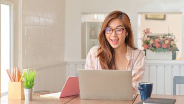 Gözlüklü kadın dizüstü bilgisayar kullanıyor ve mutlu bir şekilde gülümsüyor..