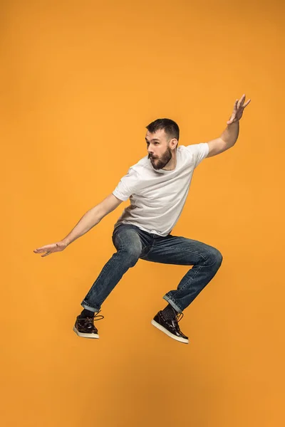 Szabadság mozgó. csinos, fiatal férfi ugrás narancssárga háttérrel — Stock Fotó